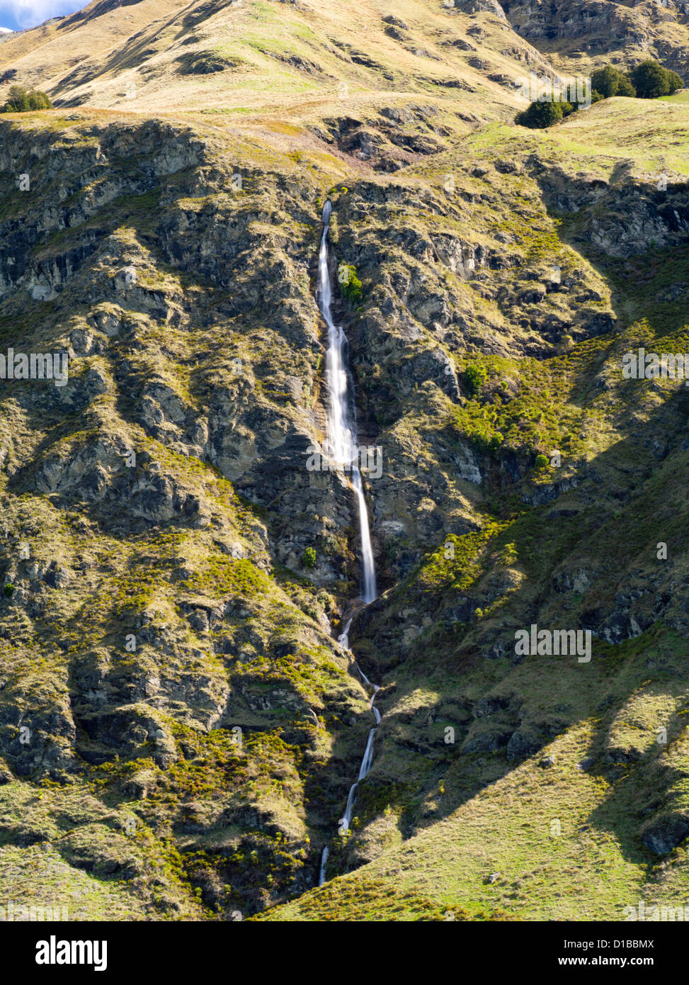 Una cascata che scorre verso il basso un aspro pendio di montagna vicino a Treble Cone ski area, Harris montagne, vicino a Wanaka, Nuova Zelanda Foto Stock