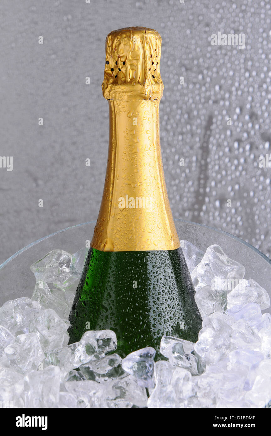 Primo piano di una bottiglia di champagne in un cristallo secchiello per il ghiaccio. Bottiglia, benna e lo sfondo sono coperti in goccioline d'acqua. Foto Stock