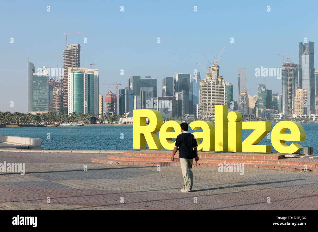 Un asiatico expat a Doha, in Qatar, passeggiate passato una moderna arte di installazione con la parola "alize' di fronte alla crescente skyline Foto Stock