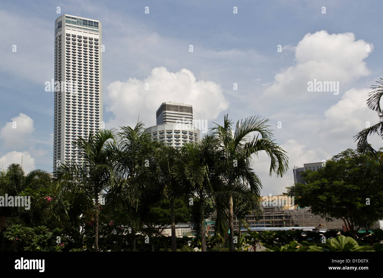 Edifici alti dietro alberi lungo con lavori di costruzione in Singapore, impostato in un cielo blu con nuvole bianche in aumento Foto Stock