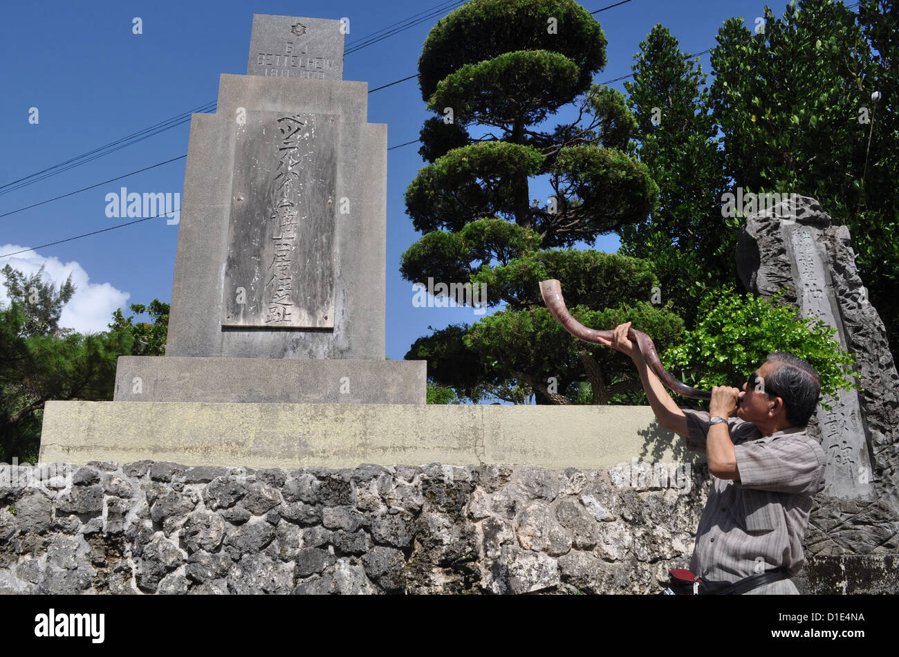(Naha Okinawa, Giappone), un uomo cristiano soffia un avvisatore acustico per onorare il missionario che ha portato il cristianesimo a Okinawa, dalla sua tomba Foto Stock