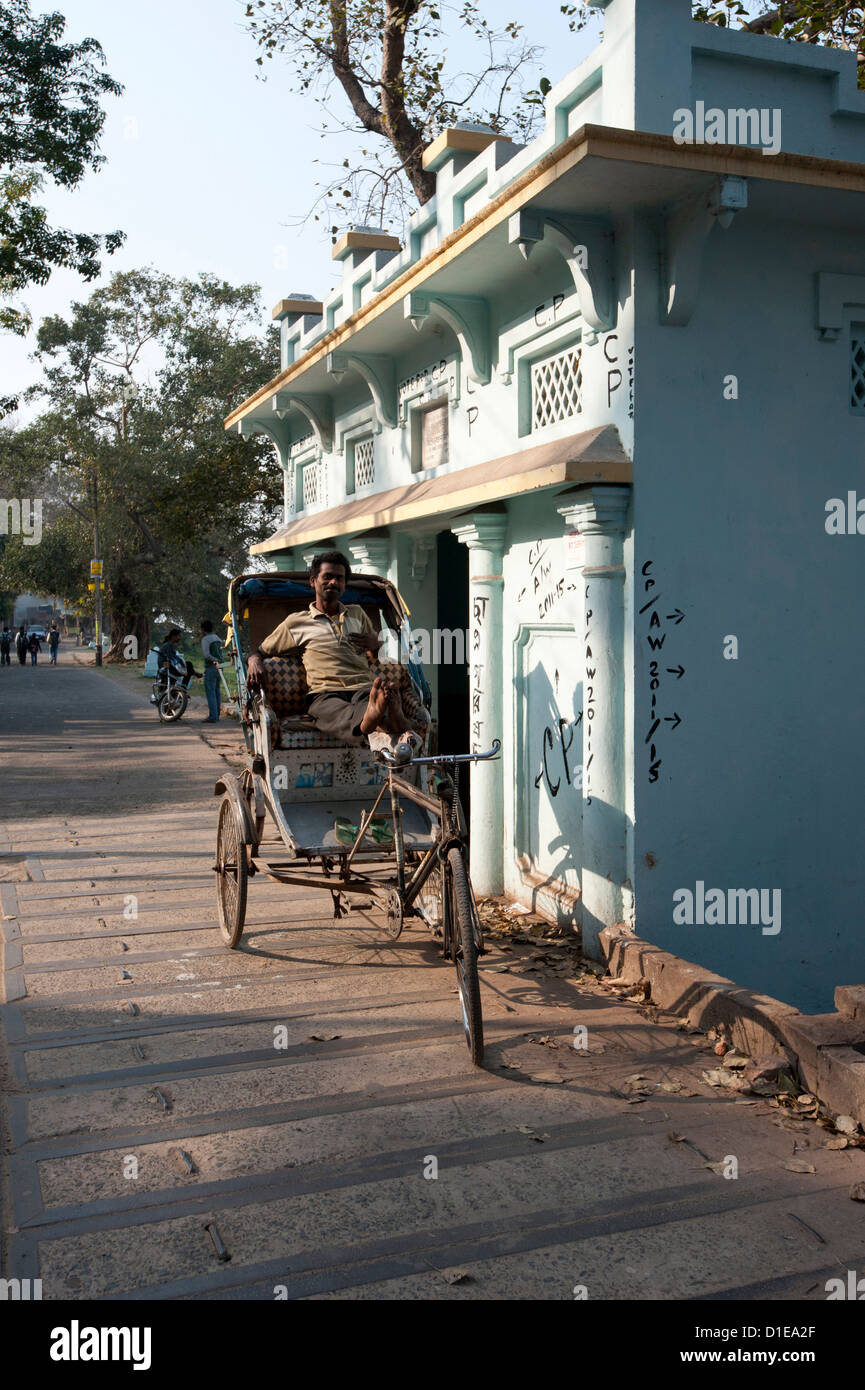 Ciclo wallah rickshaw in attesa per tariffe accanto a un santuario sulla riva del fiume, il Fiume Hooghly, Serampore, West Bengal, India Foto Stock