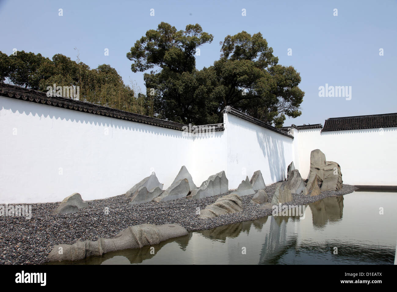 Una foto di un giardino all'interno di un cortile di un tempio Cinese. Si tratta di zen, tranquilla e calma. Vediamo alberi, acqua, muro bianco e rocce Foto Stock
