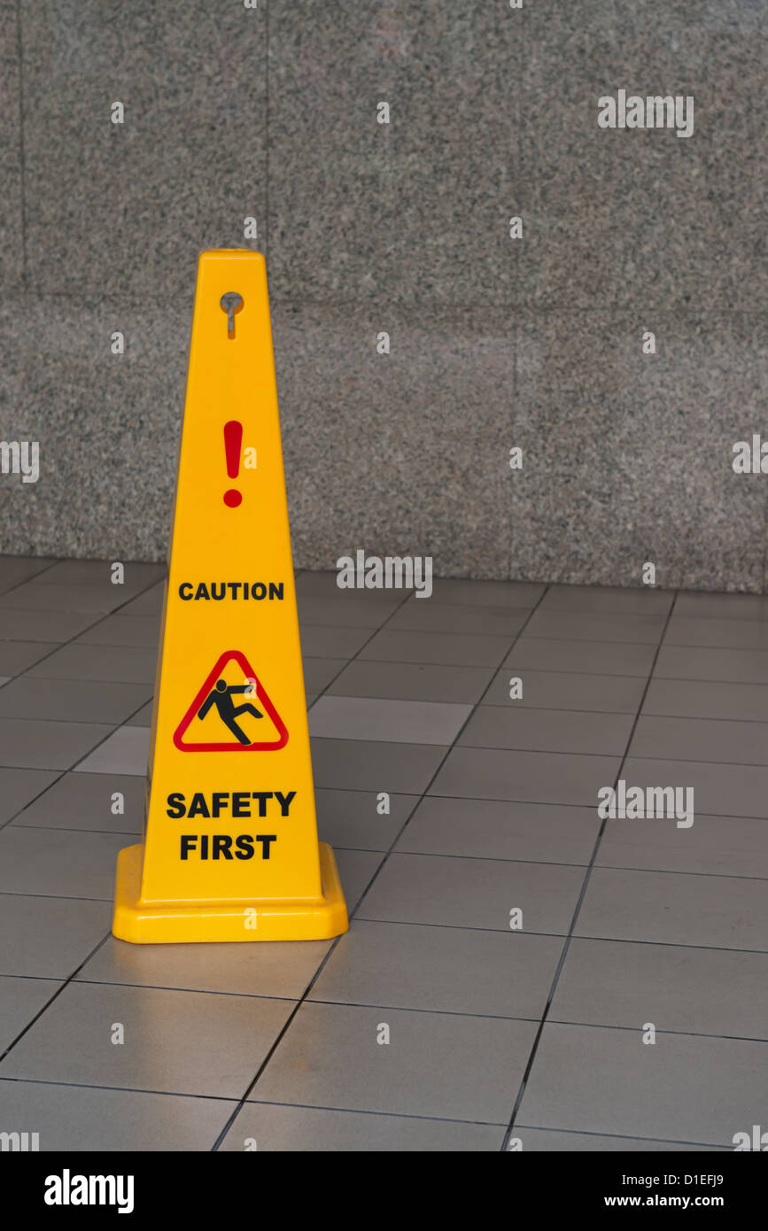 Segnale di avvertimento pavimento bagnato sul pavimento piastrellato con muro di pietra sullo sfondo Foto Stock