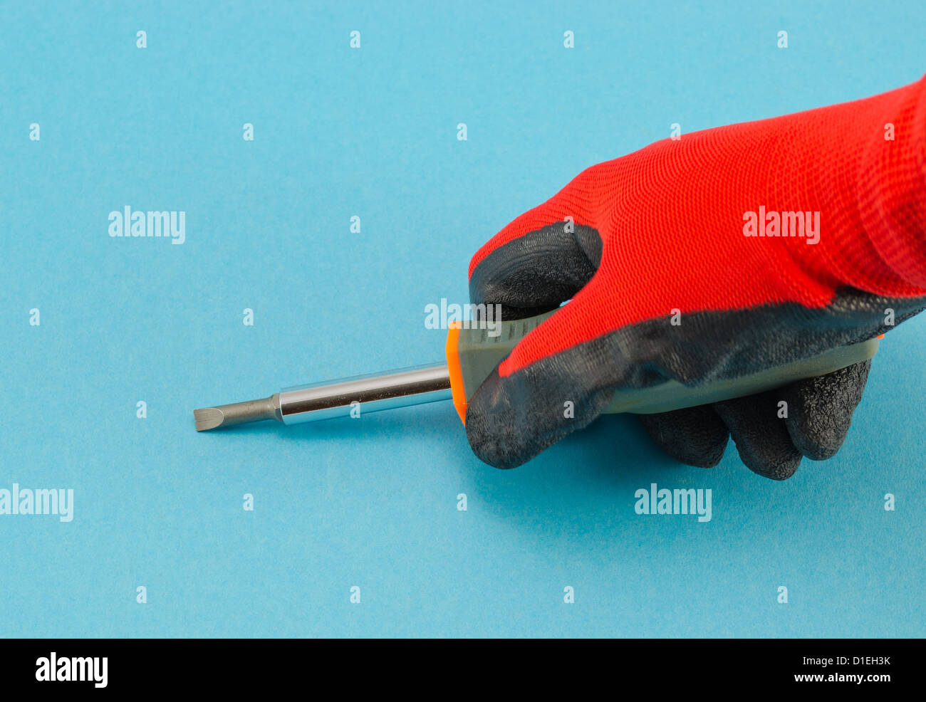 Mano con guanti arancione tenere il cacciavite su sfondo blu. Foto Stock