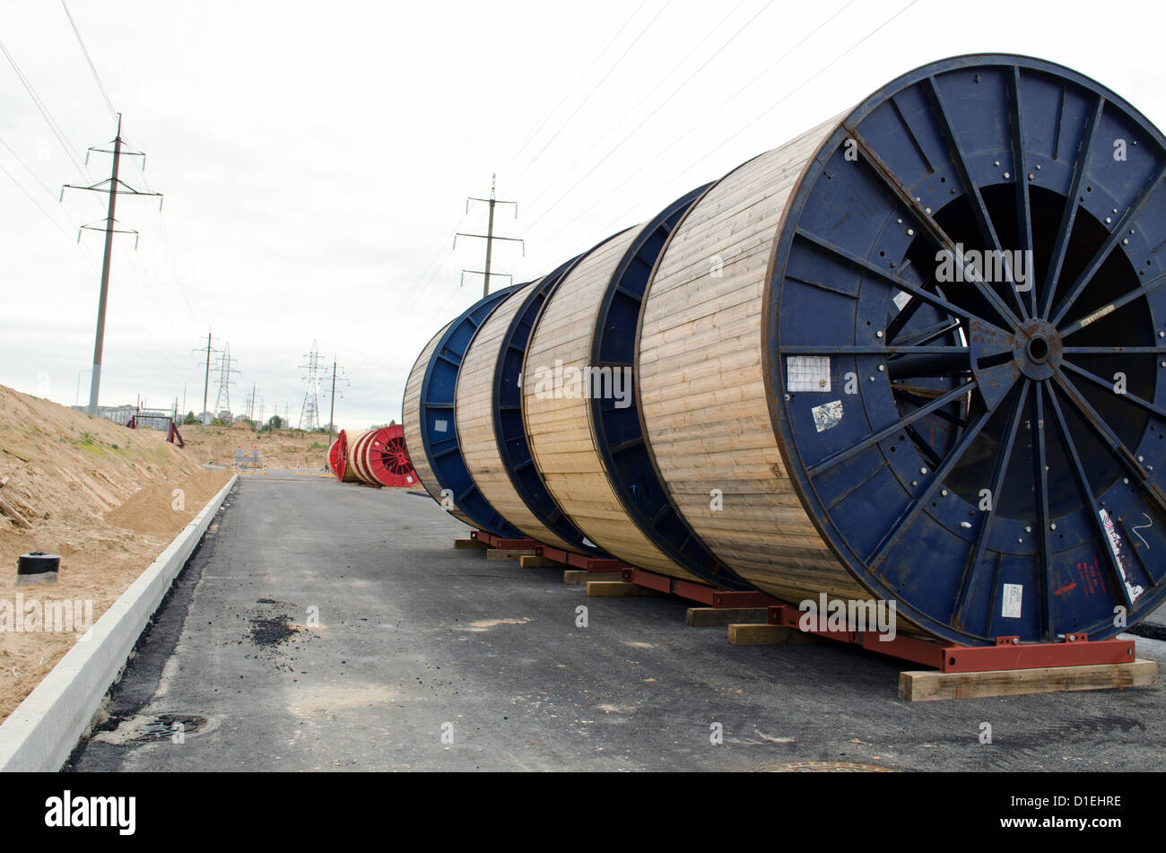 Cavo ad alta tensione delle bobine nella parte anteriore del power line sito in costruzione. la costruzione di strade e lavori di elettricità di posa della linea metropolitana. Foto Stock Cavo ad alta tensione delle bobine nella parte anteriore del power line sito in costruzione. la costruzione di strade e lavori di elettricità di posa della linea metropolitana. Foto Stock