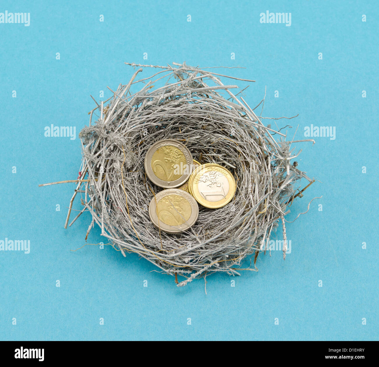 Piccolo Silver Bird Nest e monete in euro il denaro su sfondo blu. Foto Stock