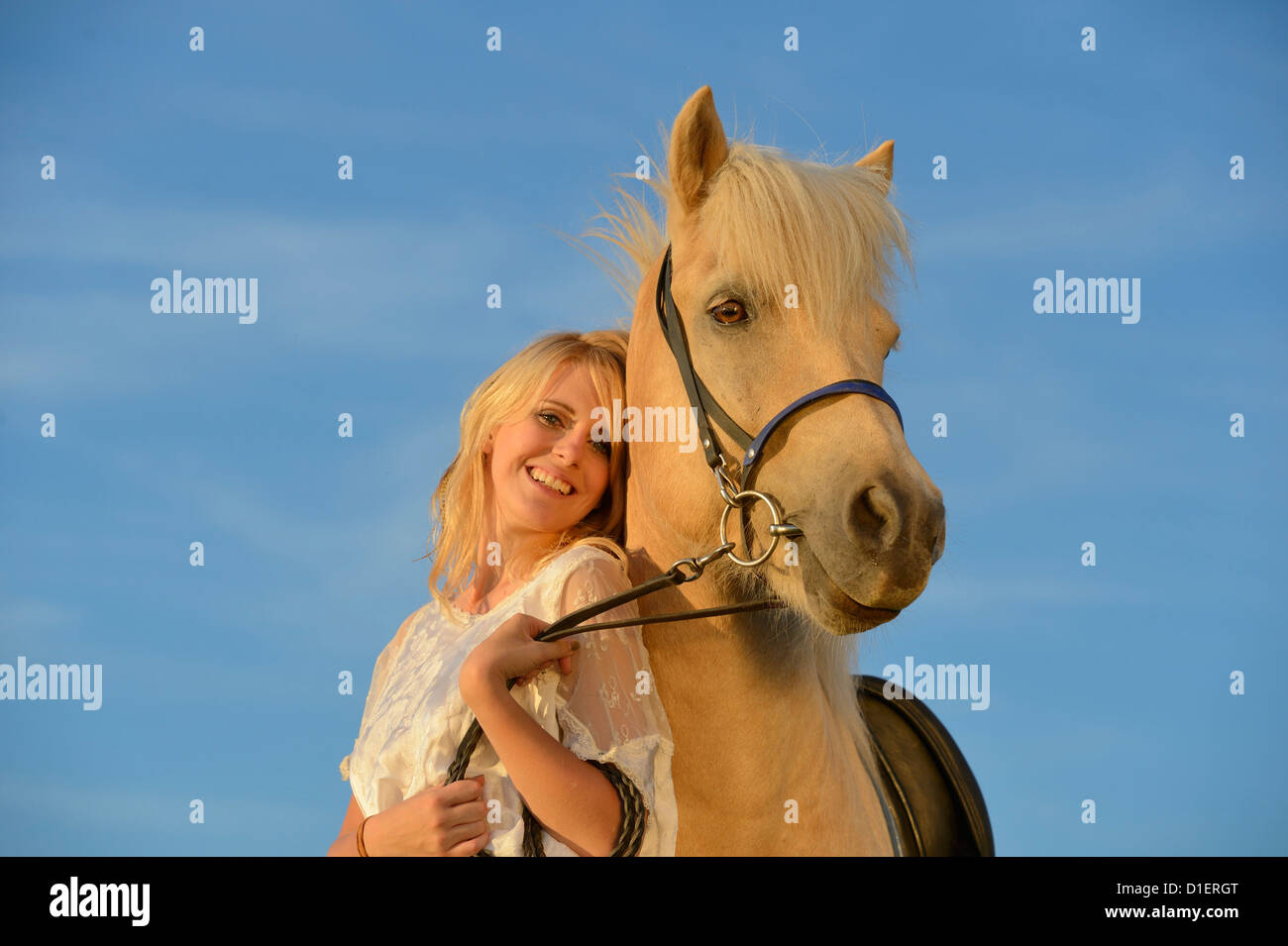 Donna sorridente in abito bianco con il cavallo sotto il cielo blu Foto Stock