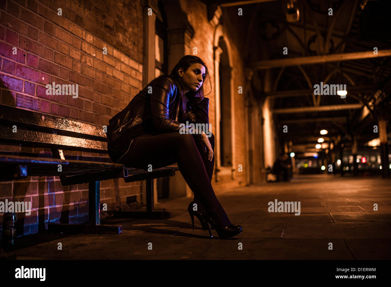 Una singola donna seduta da sola su una stazione ferroviaria piattaforma di notte nel buio in attesa di un treno REGNO UNITO Foto Stock