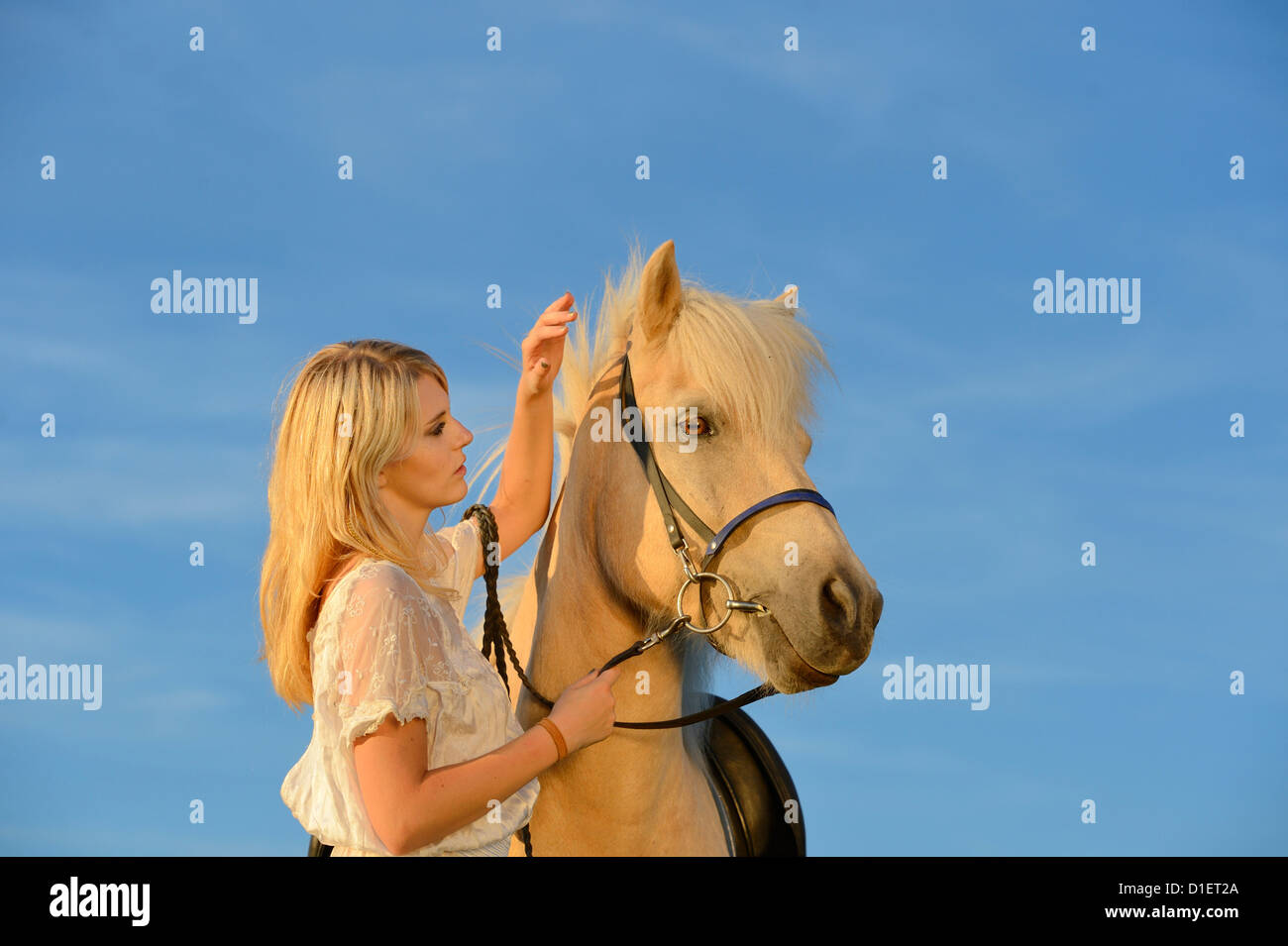 Giovane donna in abito bianco con il cavallo sotto il cielo blu Foto Stock