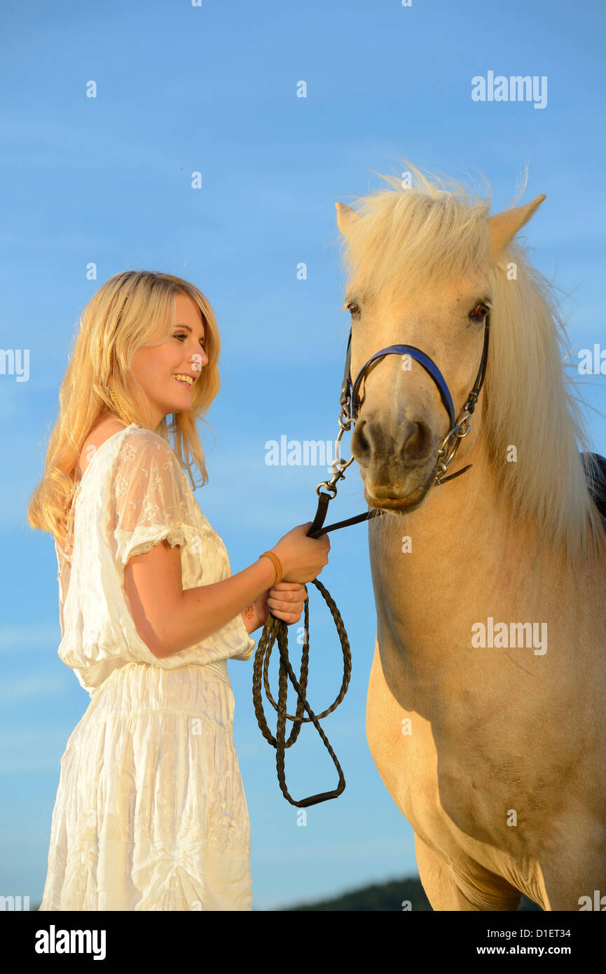 Donna sorridente in abito bianco con il cavallo sotto il cielo blu Foto Stock
