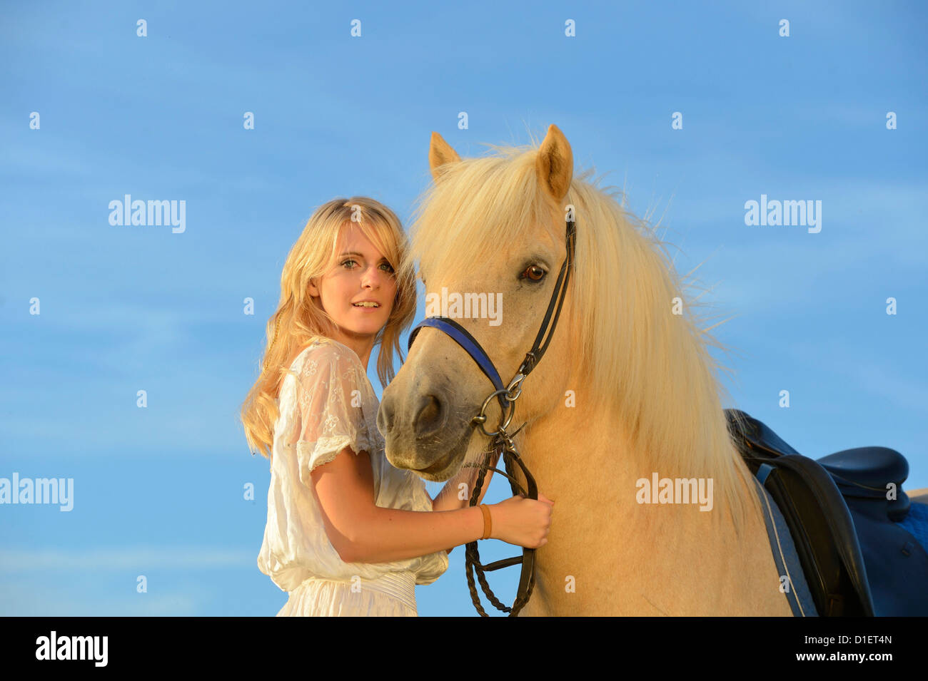 Donna sorridente in abito bianco con il cavallo sotto il cielo blu Foto Stock