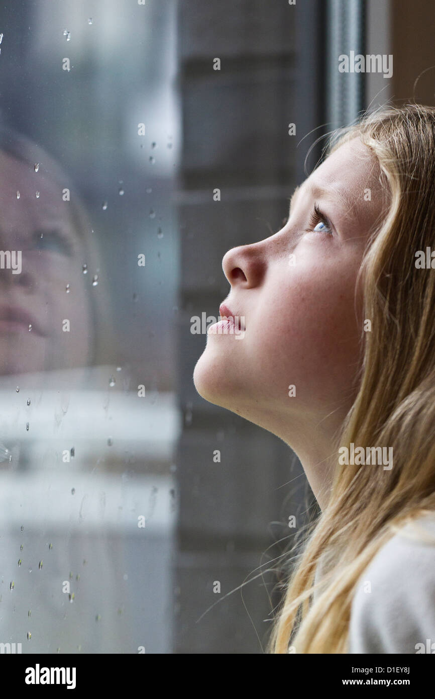 Ragazza bionda guardando fuori della finestra delle piogge Foto Stock