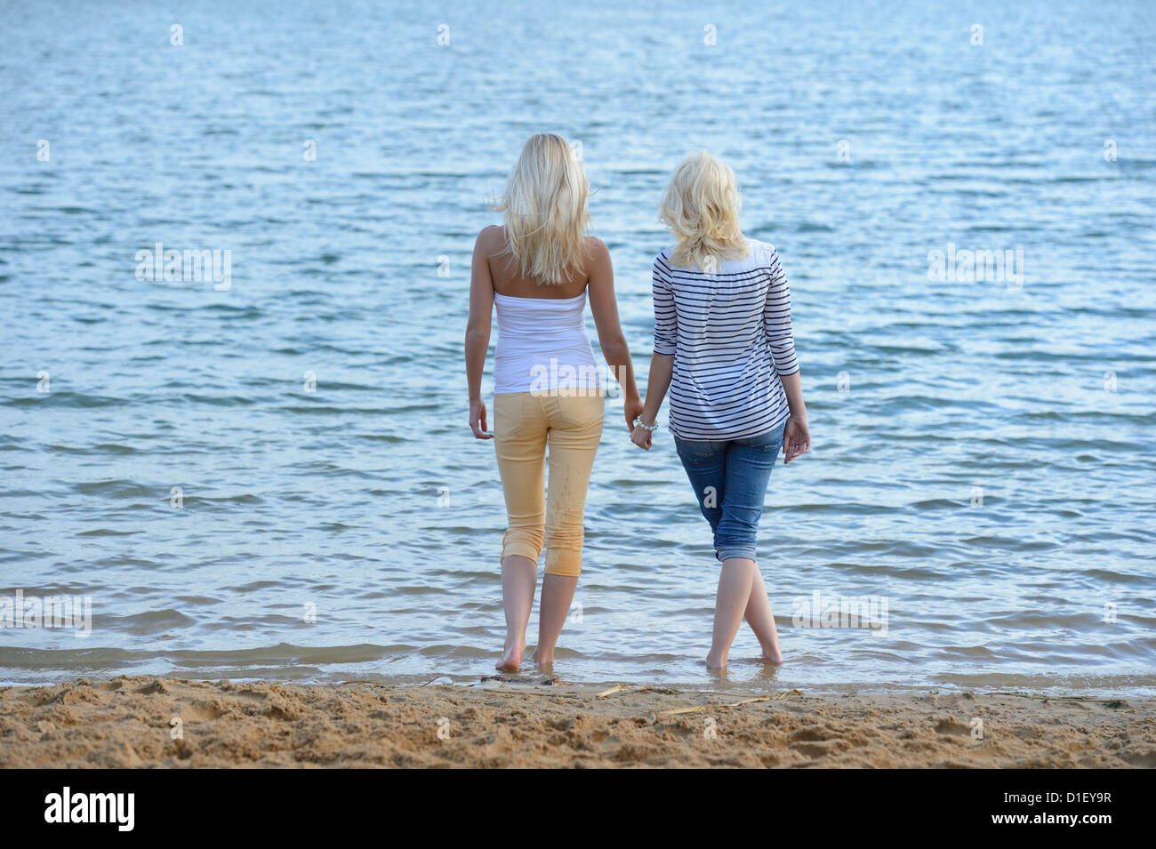 Due giovani donne bionda in piedi mano nella mano a lago balneare Foto Stock