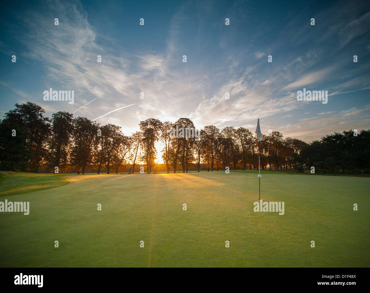 Campo da golf di sunrise, bandiera, alberi, cielo blu e nuvole. Foto Stock