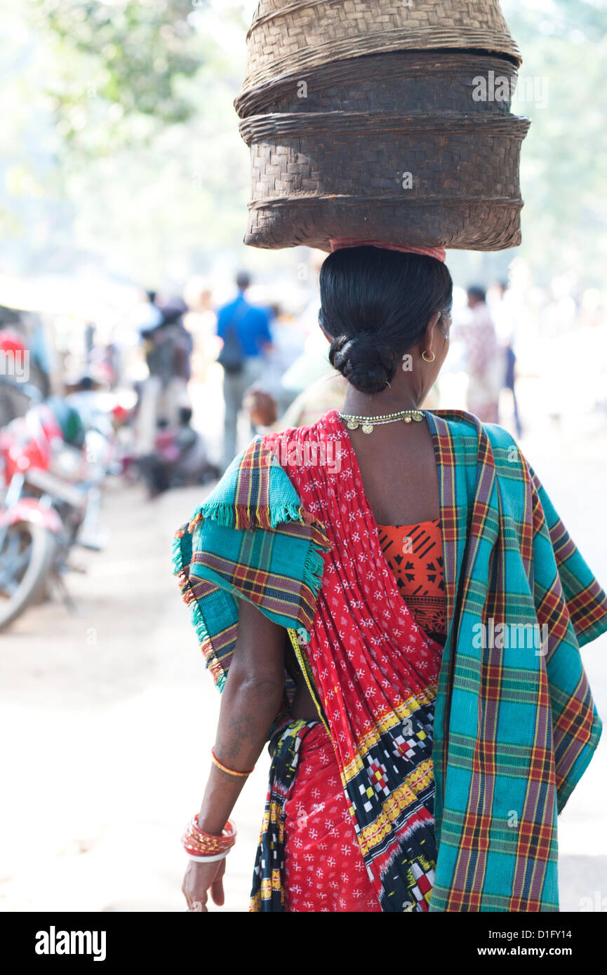 Donna al settimanale mercato tribale indossando vivacemente colorato abbigliamento e cestelli porta sulla sua testa, Bissam Cuttack, Orissa, India Foto Stock
