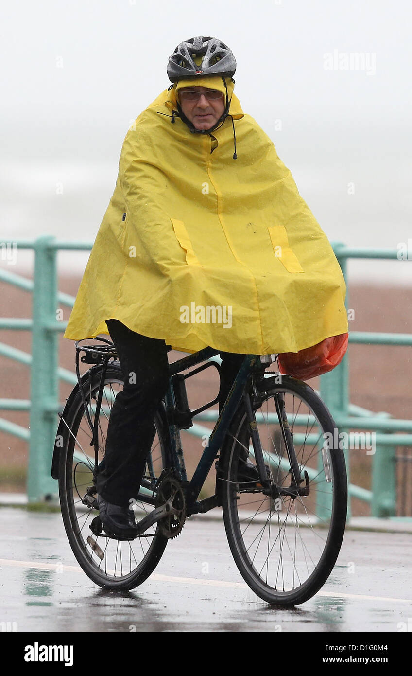 Un ciclista in un giallo brillante cicli poncho lungo Brighton Seafront sotto la pioggia battente. Foto di James Boardman Foto Stock