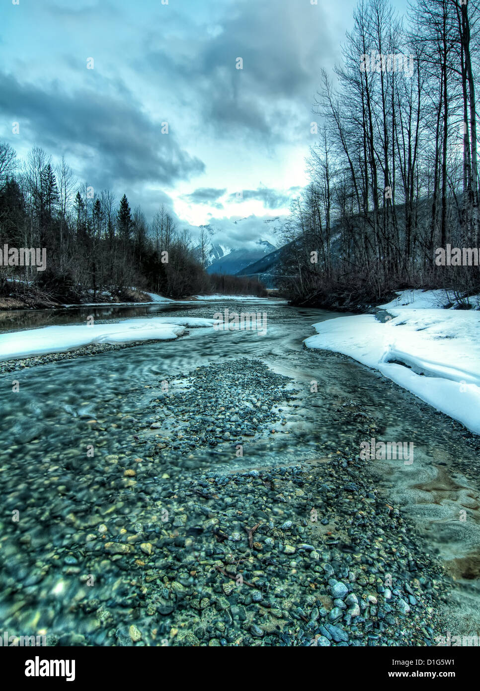 Creek rivestita con la neve ha un tono freddo e le montagne in distanza. Foto Stock