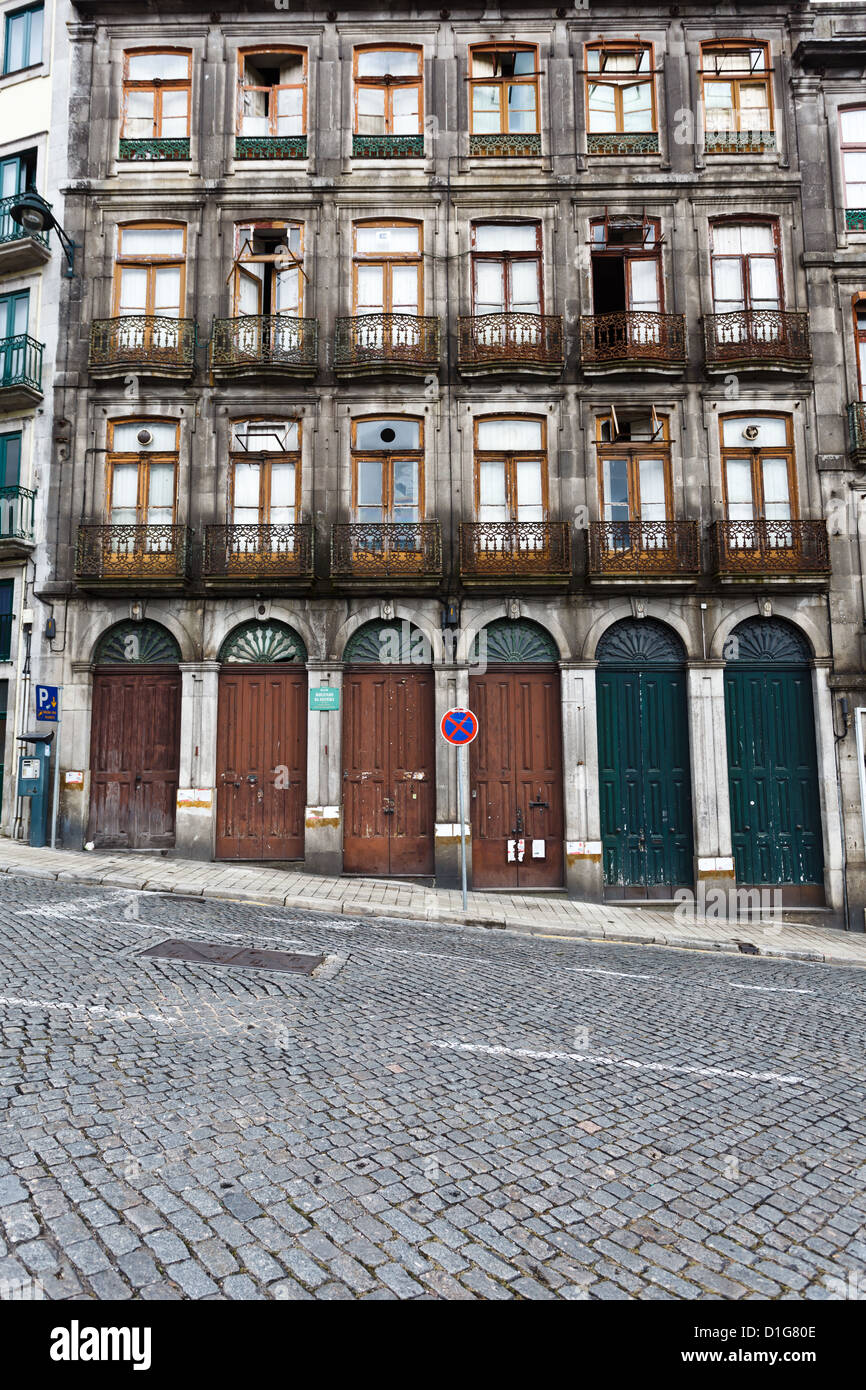 Facciata di un condominio che mostra porte al piano terra che diventano sempre più alte su una strada ripida in pendenza a Porto, Portogallo. Foto Stock