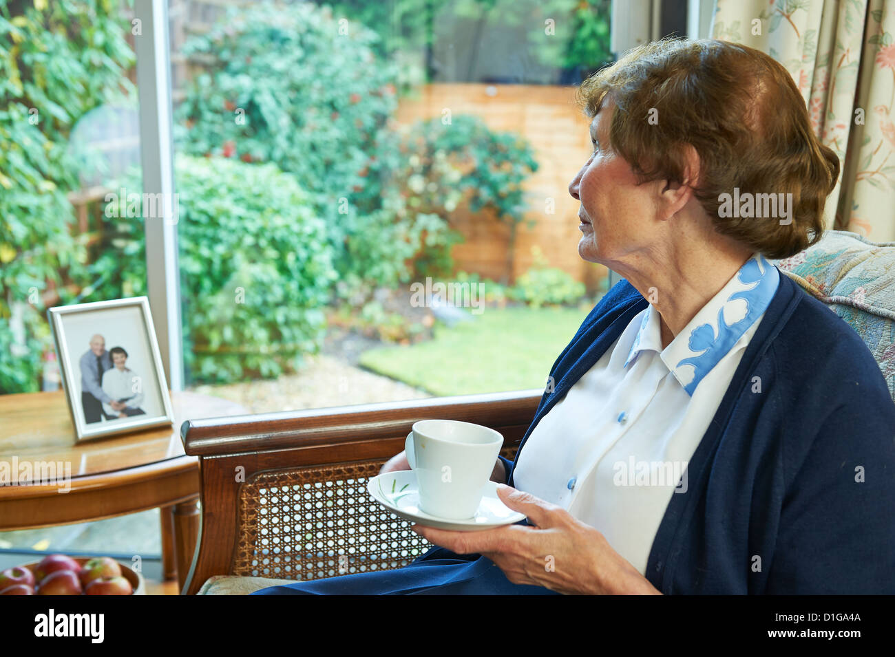 Senior old Lady guardando fuori della finestra purtroppo con una fotografia del suo defunto marito e lei stessa insieme Foto Stock
