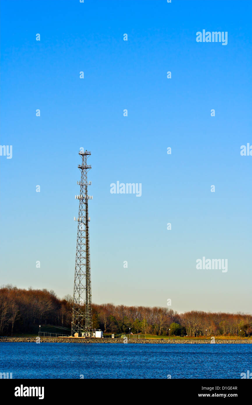 Una torre di comunicazione sul bordo di un lago con un cielo azzurro come sfondo. La foto è in verticale o in formato ritratto. Foto Stock