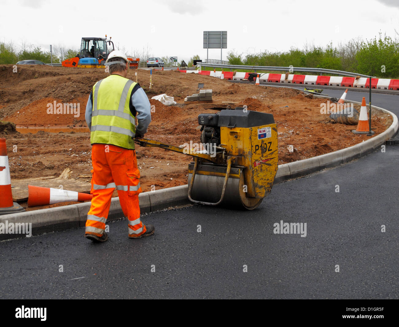 Roadworker operazione a semovente rullo sul manto di pietrischetto bitumato asfalto asfalto affioramento di nuova strada nel Regno Unito Foto Stock