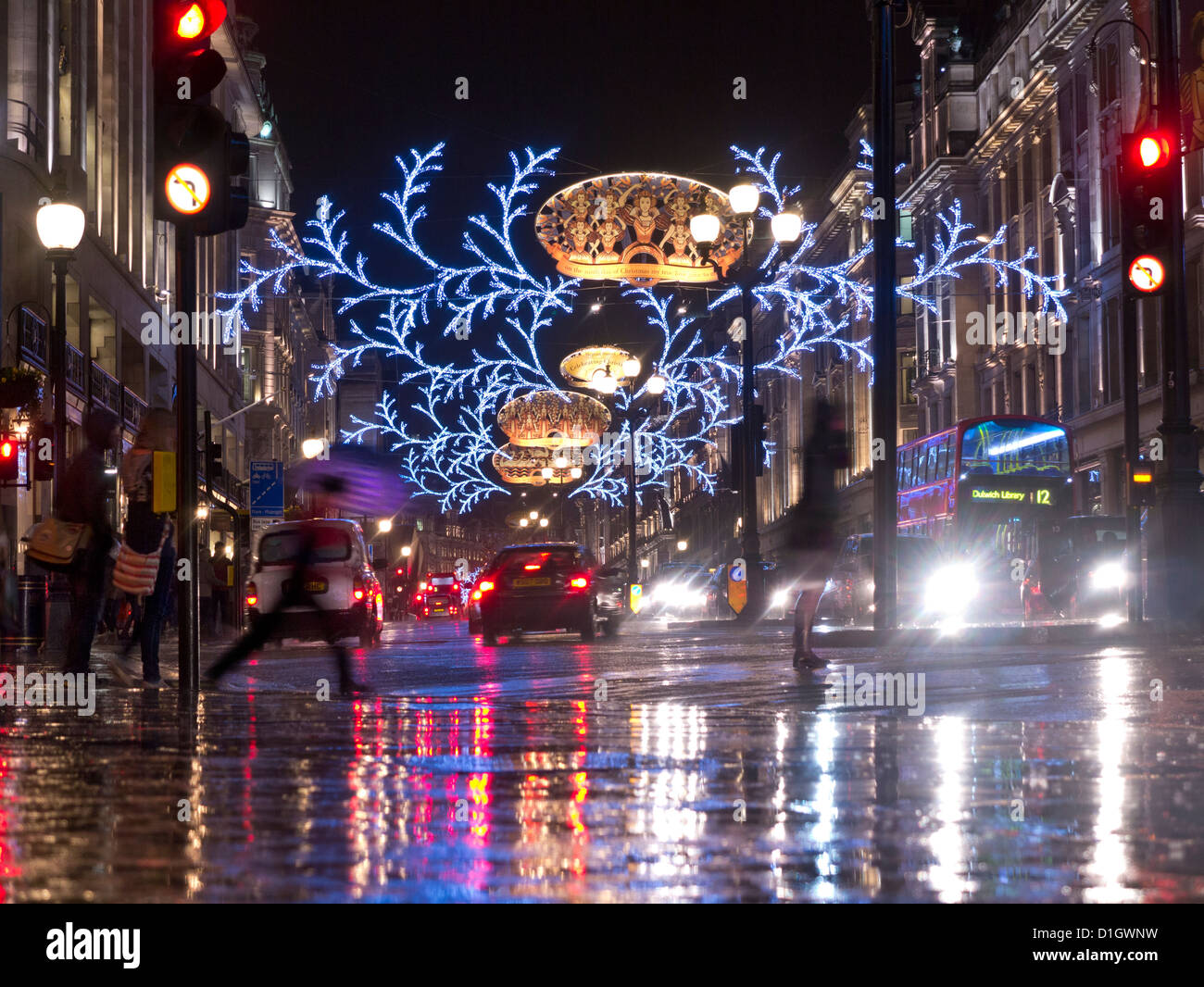 Occupato la scena del Natale shoppers, traffico e ombrelloni in una pioggia spazzata di Regent Street con le luci di Natale dietro London REGNO UNITO Foto Stock