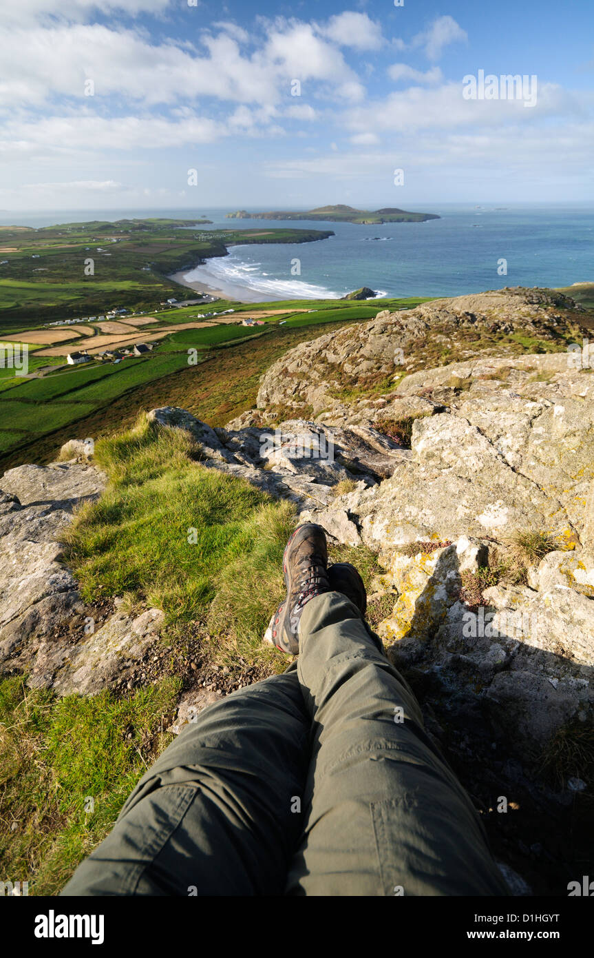 Prospettiva in prima persona con gambe di telespettatori nel telaio dal punto più alto sulla St Davids testa, Carn Llidi su una bella mattina di sole. Foto Stock