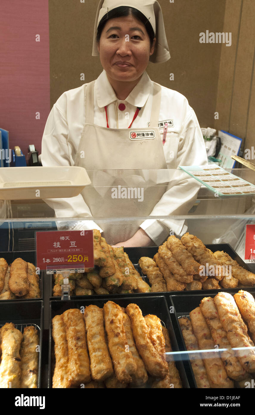 Una donna assistente vendite vendita snack fritti alimenti ad una stazione ferroviaria in Giappone Foto Stock