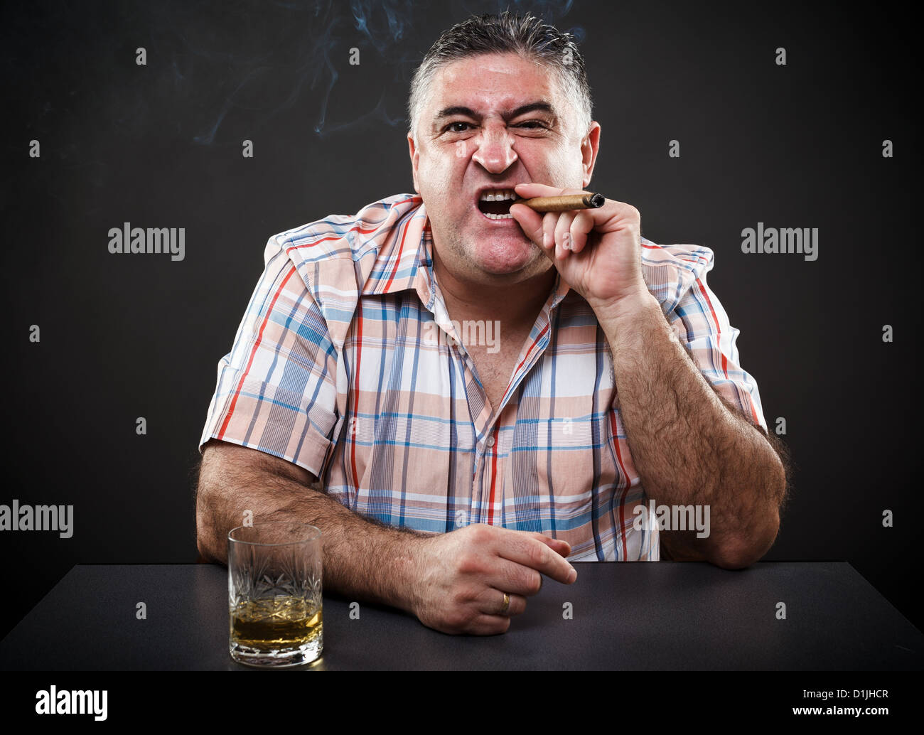 Ritratto di una matura mafioso di bere e fumare durante la seduta a tavola su sfondo grigio Foto Stock
