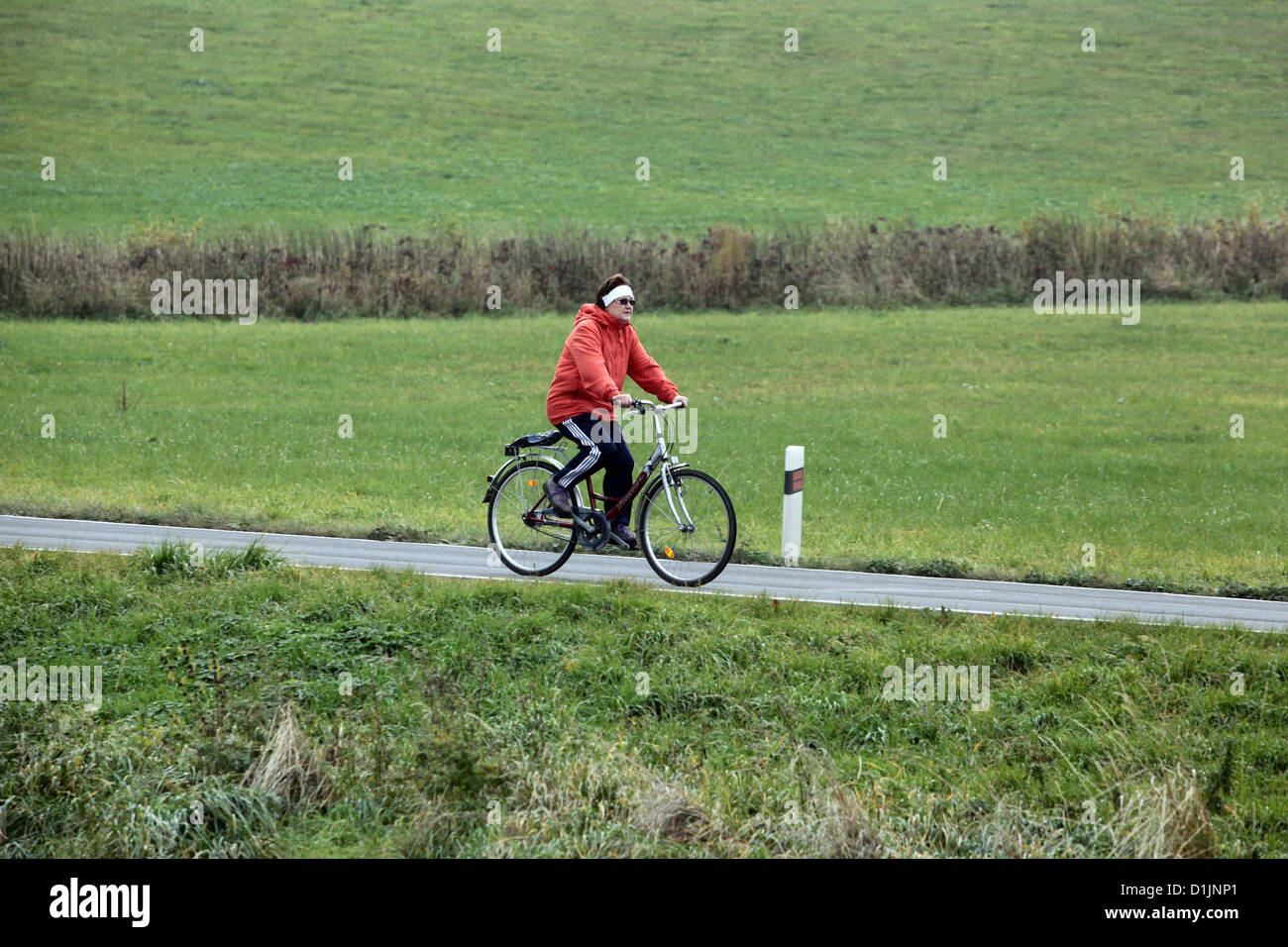 Donna anziana in bicicletta da sola sulla strada rurale, giacca rossa Repubblica Ceca Europa donna in bicicletta da sola fuori Foto Stock