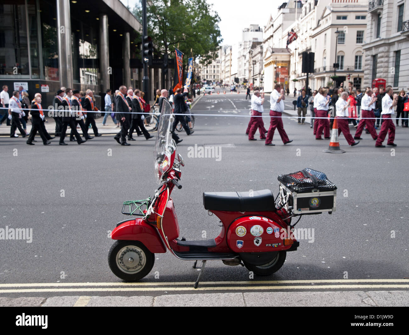 Un arancio fine marzo attraverso le strade di Londra, durante l'estate del 2012. Un rosso Vespa è parcheggiato in primo piano. Foto Stock