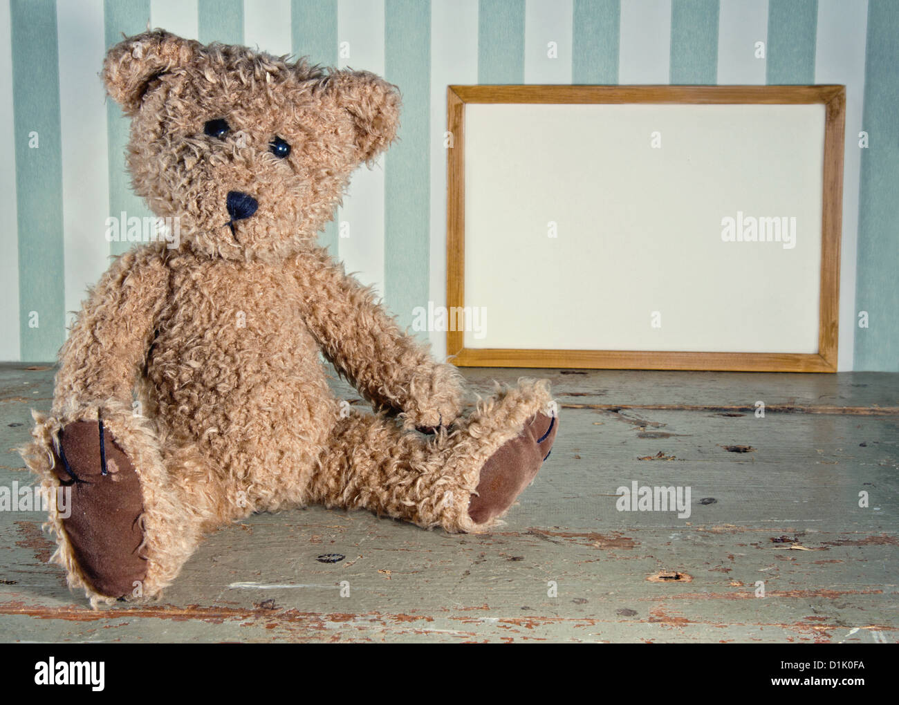 Impostazione vintage del vecchio orsacchiotto seduto accanto a un vuoto di telaio in legno per lo spazio di copia Foto Stock
