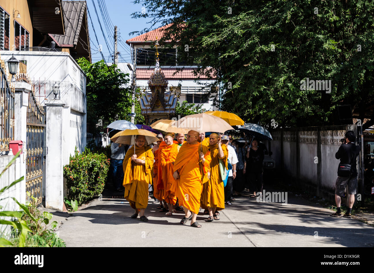 I monaci buddisti che indossa luminosa arancione vesti e portante ombrelloni condurre il corteo funebre con alte galleggiare su strada Foto Stock