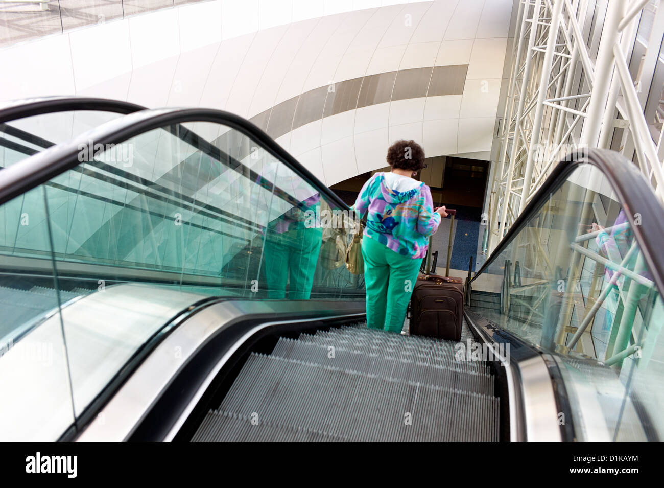 Una donna sovrappeso in colori appiccicoso scorre giù per la scala mobile in un aeroporto Foto Stock