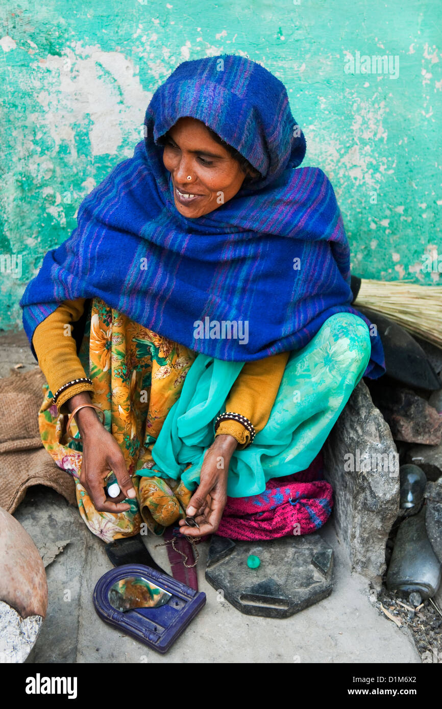 Una donna indiana in uno scialle blu si trova al di fuori della propria casa contro un muro verde di applicare il make up del mattino in Rajasthan in India Foto Stock