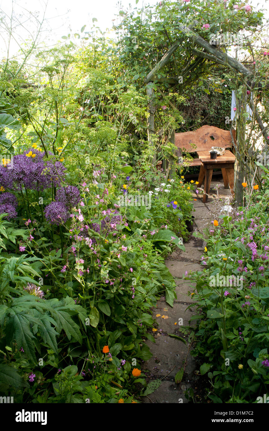 Sentiero lastricato che conduce attraverso piante erbacee inizio estate frontiere alla zona relax, Agriturismo Cottage Foto Stock