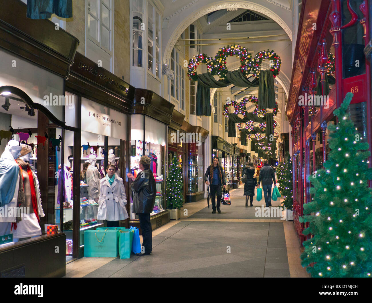 Burlington Arcade a Piccadilly con tradizionali decorazioni natalizie e agli acquirenti con shopping bags London REGNO UNITO Foto Stock