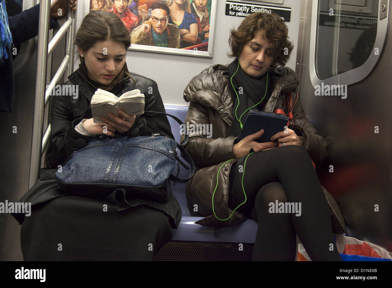 Giovane ebrea legge da un ebreo libro di preghiera mentre un'altra donna legge dal suo tablet a Brooklyn un treno della metropolitana, NYC. Foto Stock