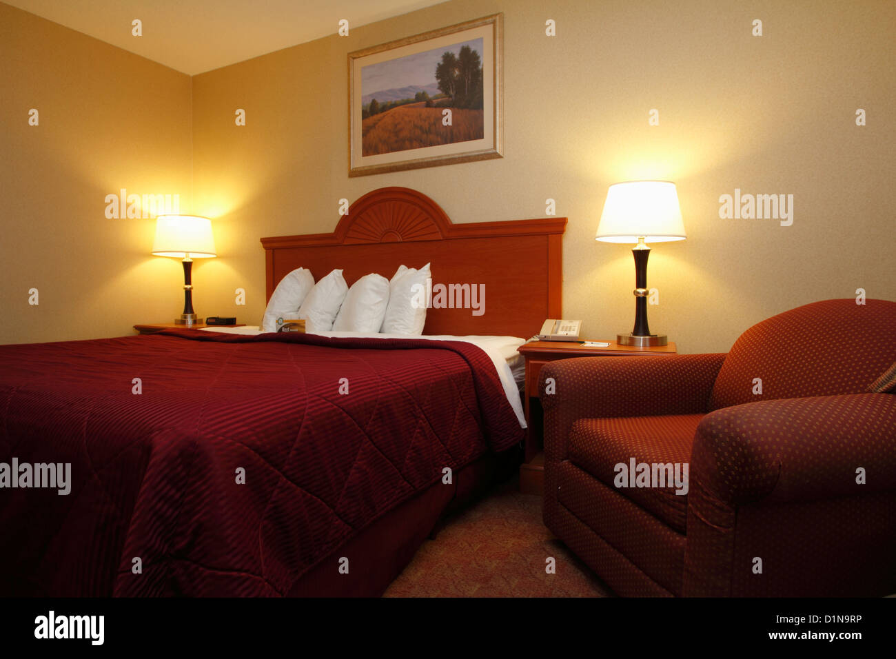 Un tipico hotel del Nord America o la stanza del motel che mostra un letto di dimensione king ed una poltrona così come lampade e quattro cuscini Foto Stock