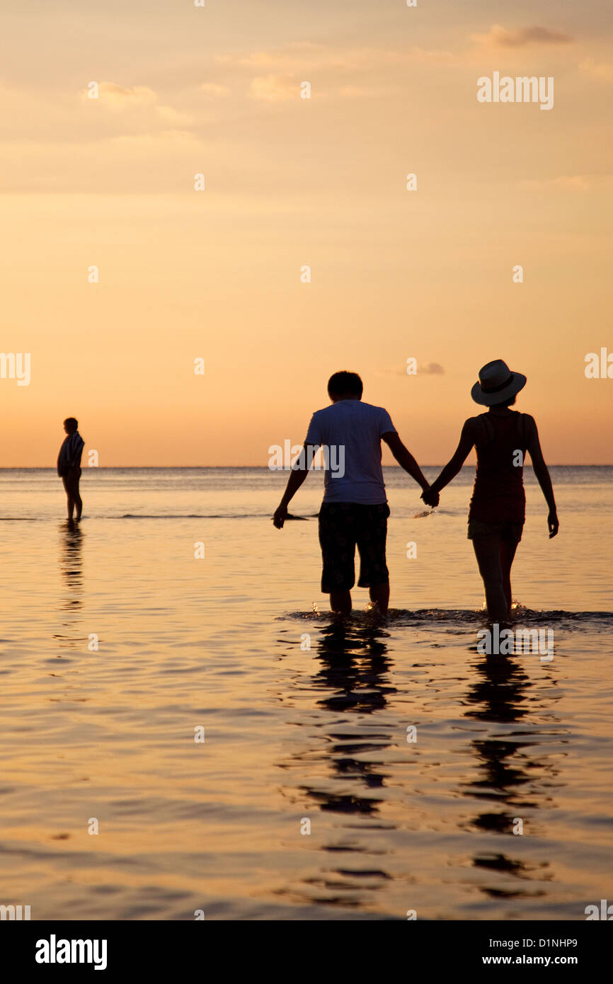 Una giovane coppia entra in acqua e tiene le mani dopo il tramonto sulla spiaggia di Lovina, Bali, Indonesia Foto Stock