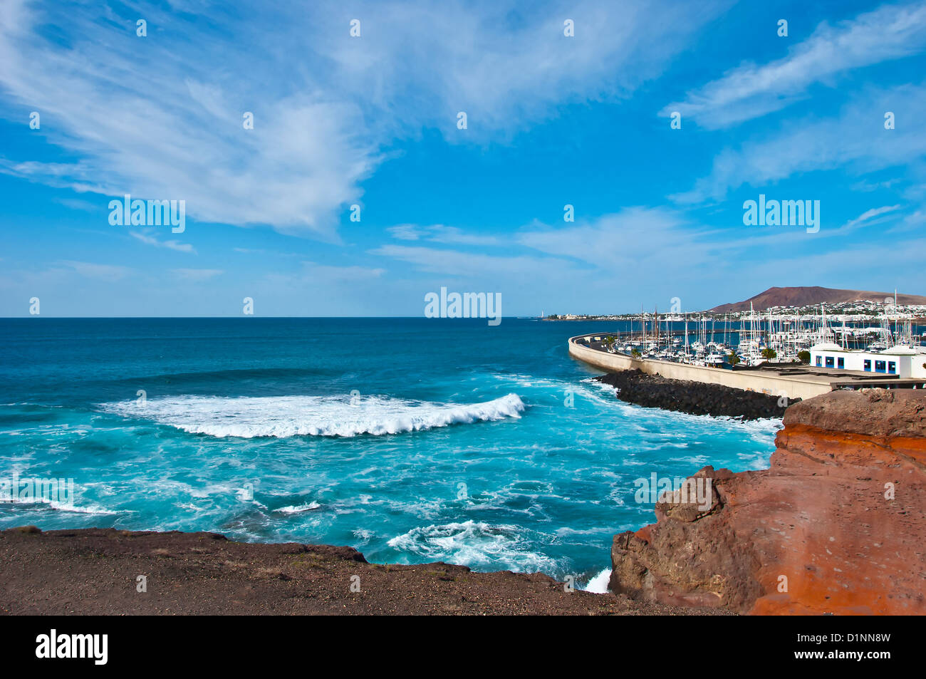 La rottura dell'Atlantico sulla costa vicino a Playa Blanca Lanzarote sotto un blu cielo invernale con cirrus nuvole Foto Stock
