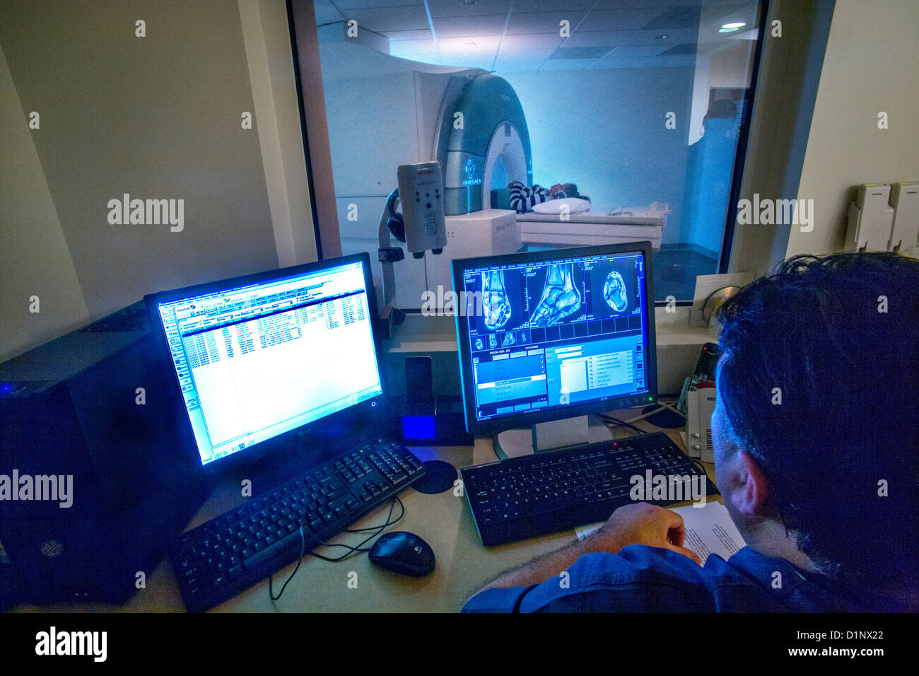 Visto attraverso una finestra in vetro di sicurezza ragazza adolescente i feriti della caviglia viene esaminata utilizzando un Siemens 3T Vario MRI. Foto Stock