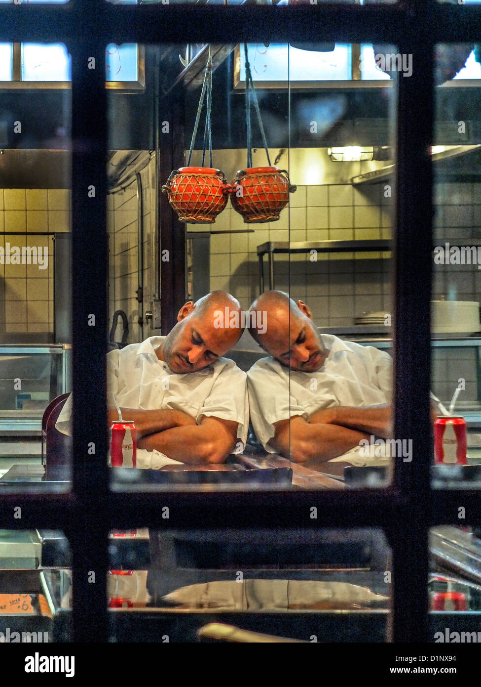 Una stanca African American cook è riflessa in uno specchio a muro come egli dorme dopo la chiusura ristorante a tarda notte in Brooklyn. Foto Stock
