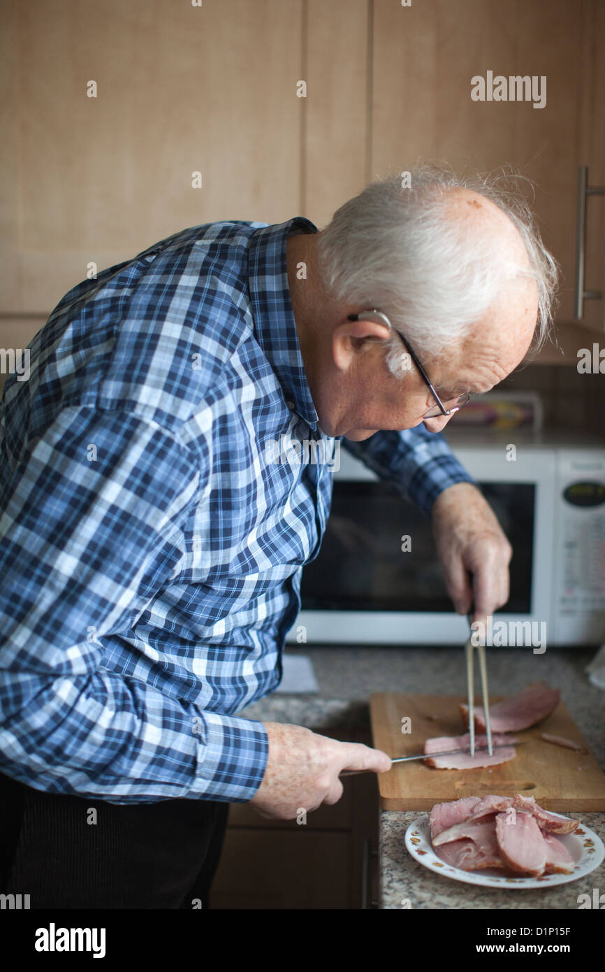 Titolare di pensione o di rendita il taglio di una fetta di prosciutto per il pranzo nella cucina di casa, England, Regno Unito Foto Stock