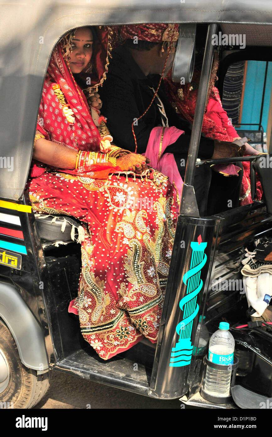 Una sposa colorati abiti da sposa sul suo modo di celebrare il suo matrimonio che viaggiano in riscio' o tuc-tuc guarda pensieroso in India Foto Stock