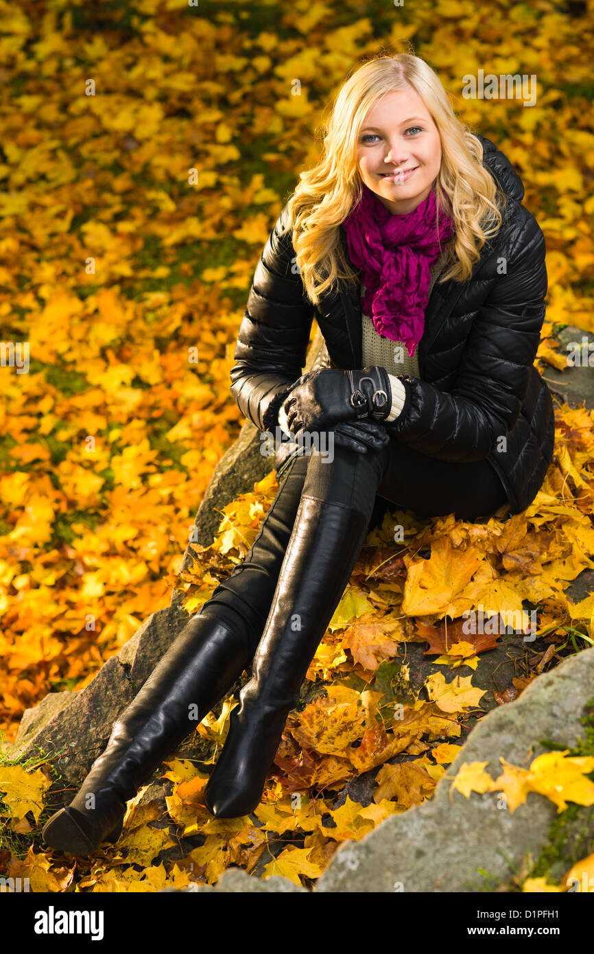 Bella ragazza seduta su una roccia, Colore di autunno lascia sullo sfondo, formato verticale Foto Stock