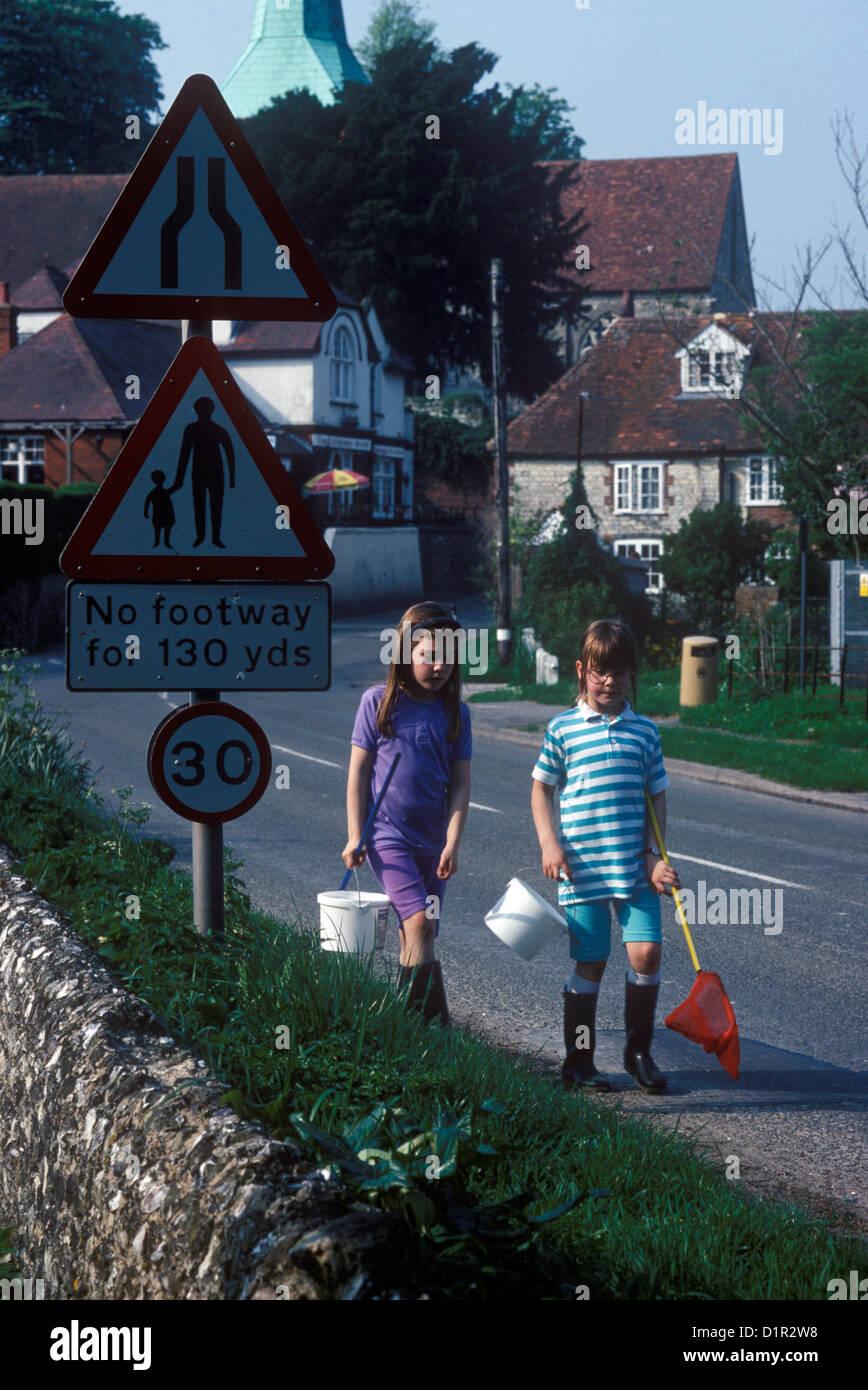 I bambini a piedi lungo una strada di campagna attraverso un villaggio con le loro reti da pesca Foto Stock