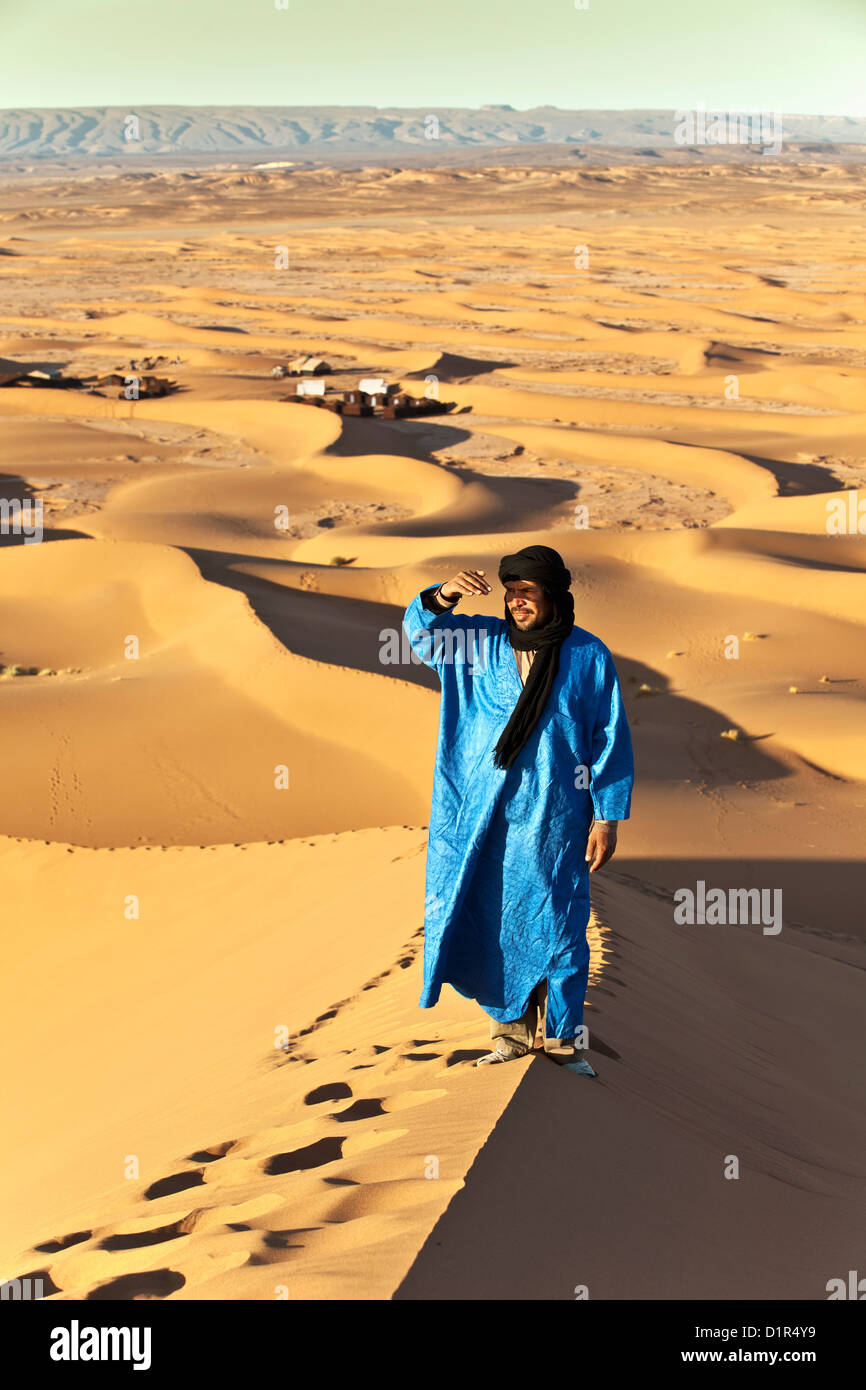 Il Marocco, M'Hamid, Erg Chigaga dune di sabbia. Deserto del Sahara. Local Berber uomo sulla duna di sabbia, sfondo tourist camp, bivacco. Foto Stock