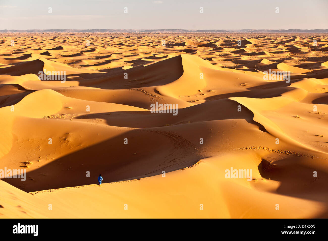 Il Marocco, M'Hamid, Erg Chigaga dune di sabbia. Deserto del Sahara. Local Berber uomo sulla duna di sabbia, sfondo tourist camp, bivacco. Foto Stock